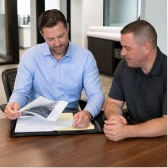 A contractor and customer reviewing a roofing estimate at a table.