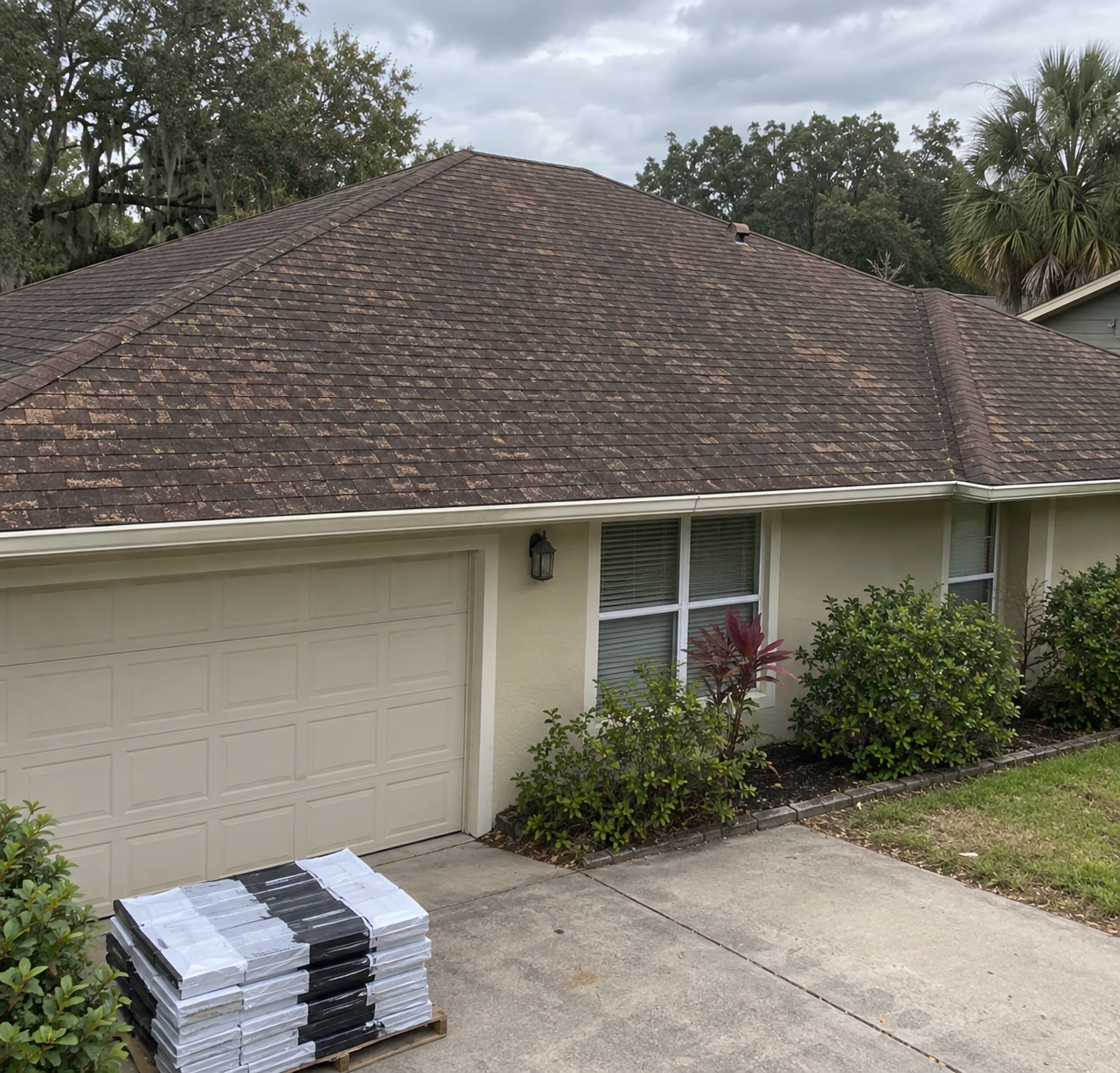 House with a shingle roof and roofing materials in the driveway.