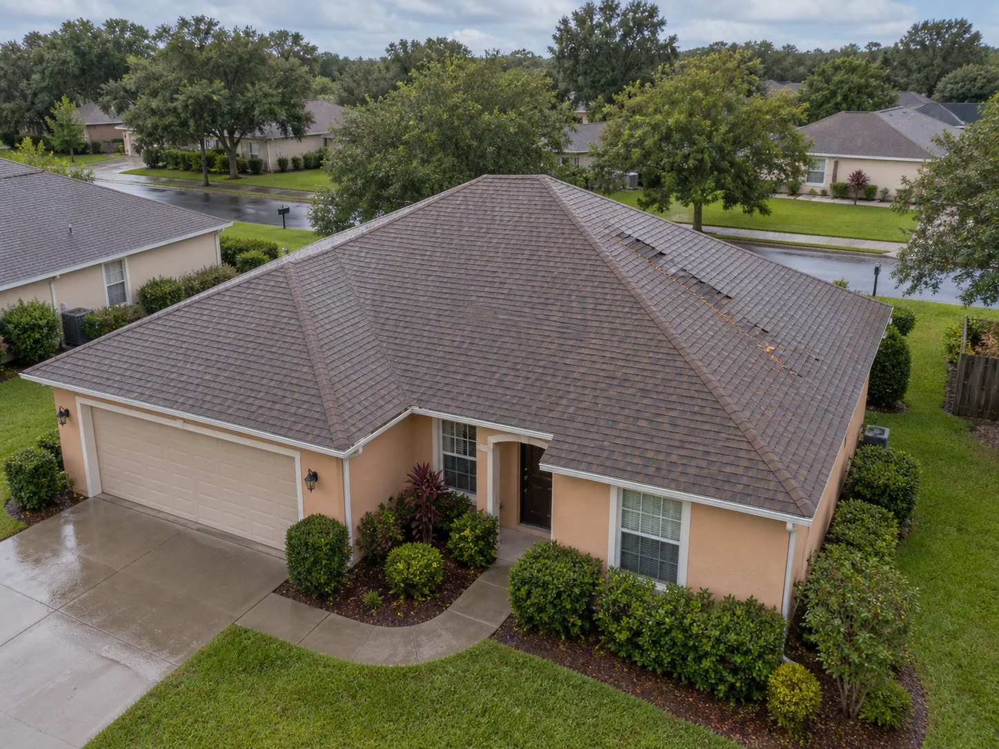 An intact hip roof with localized shingle displacement and scattered leaf debris.