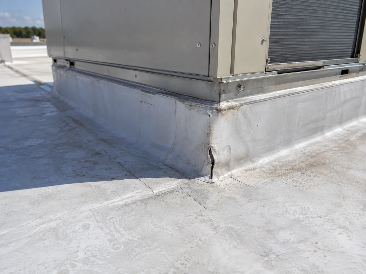 Localized membrane flashing split at a rooftop equipment curb.