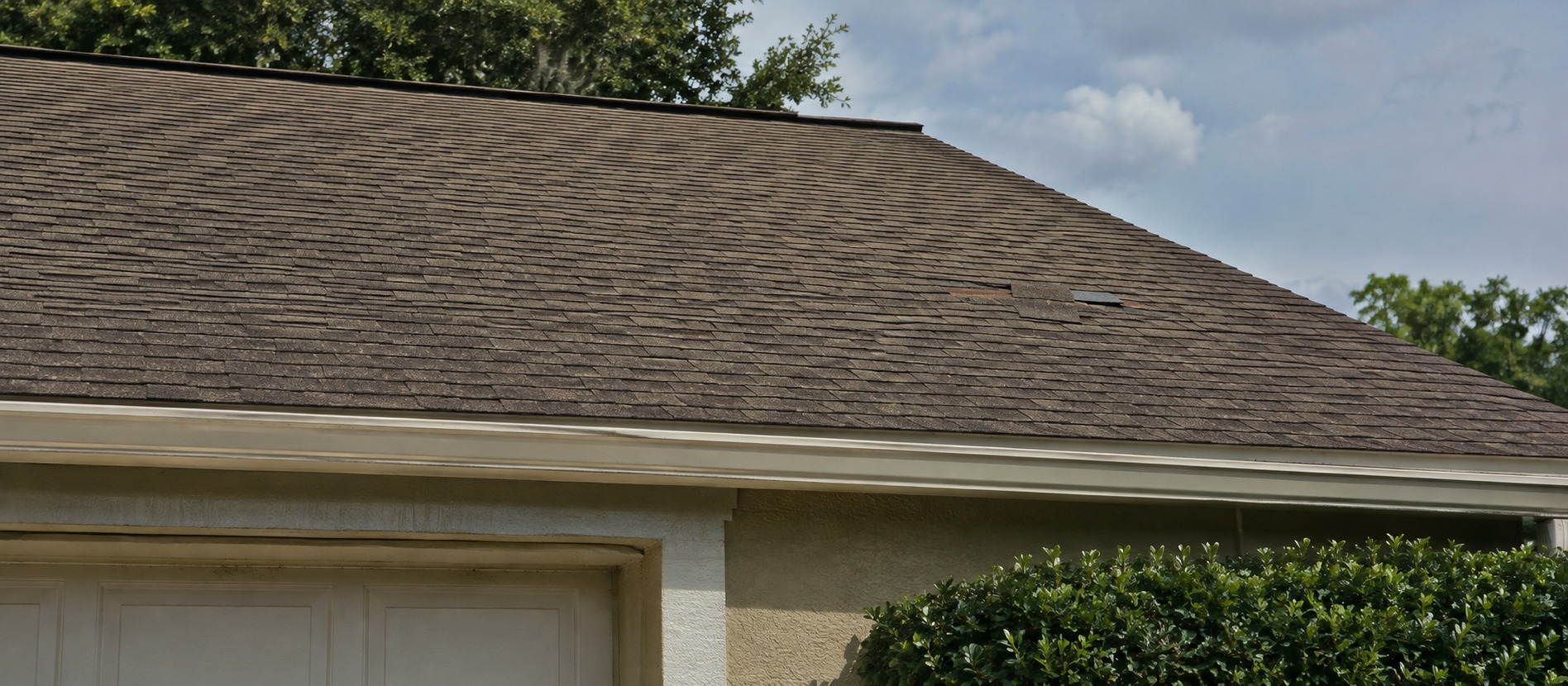 A patch of missing shingles on the roof above a garage.