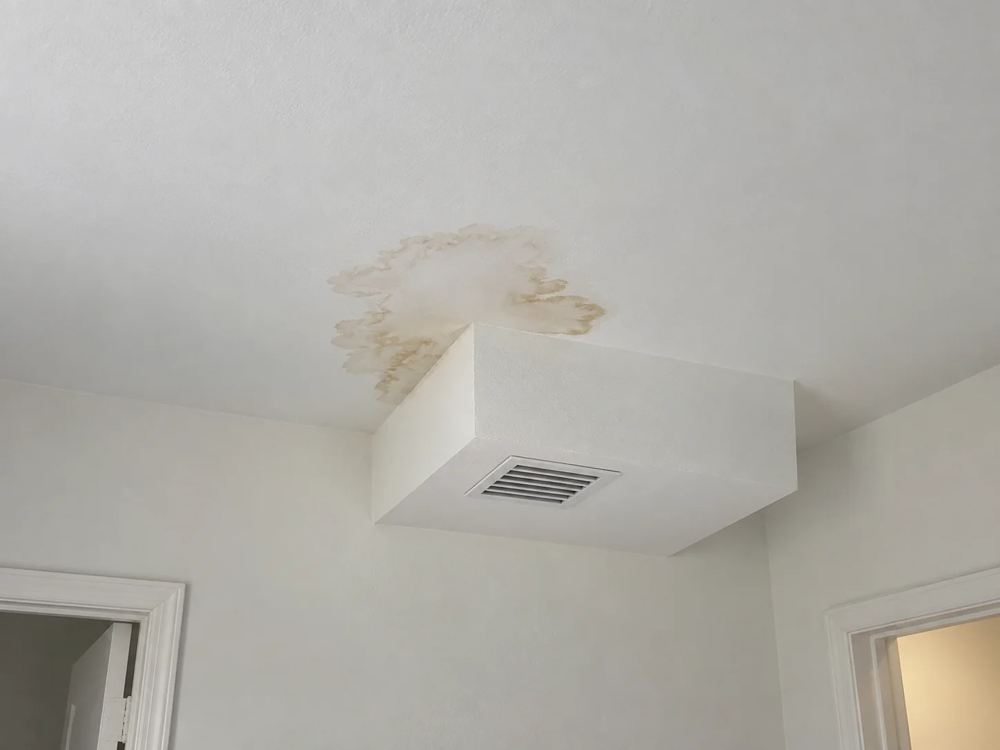 An irregular ceiling stain beside a boxed-in vent chase.