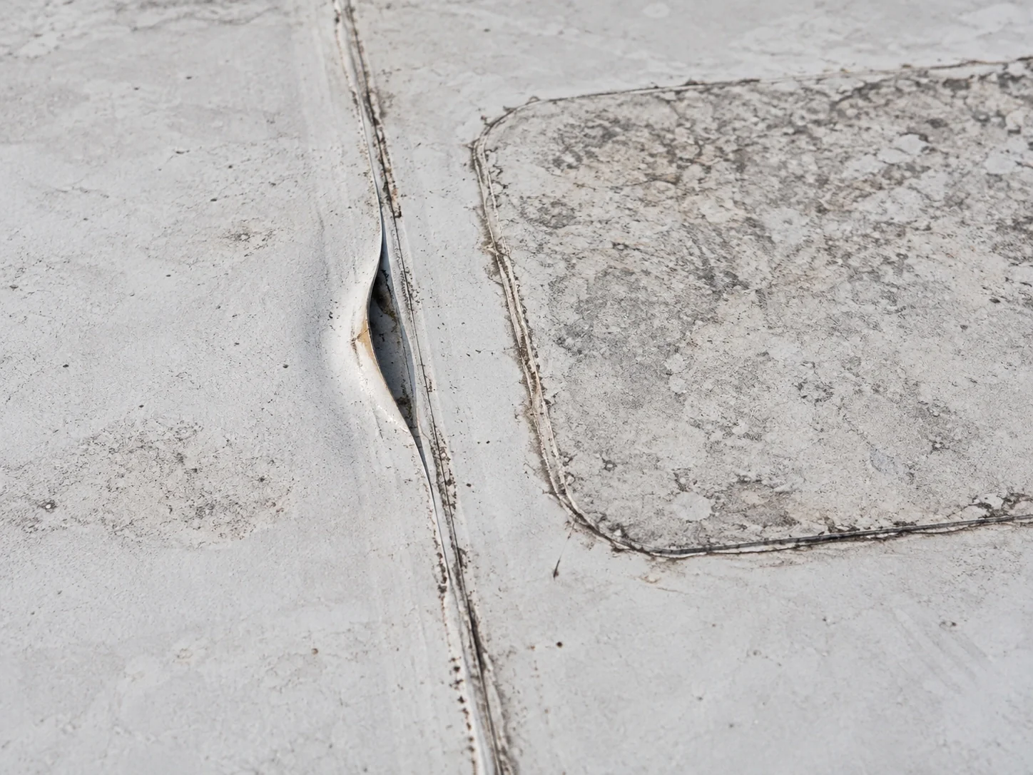 Lifted commercial roof seam beside an older membrane patch.