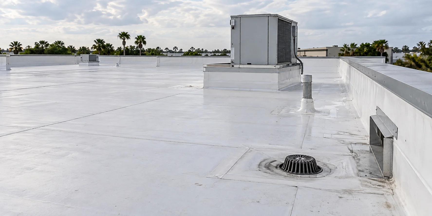 White commercial roof membrane with seams, a drain and rooftop equipment.