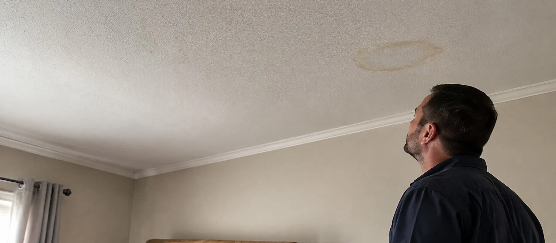 A person examining a water stain on an interior ceiling.