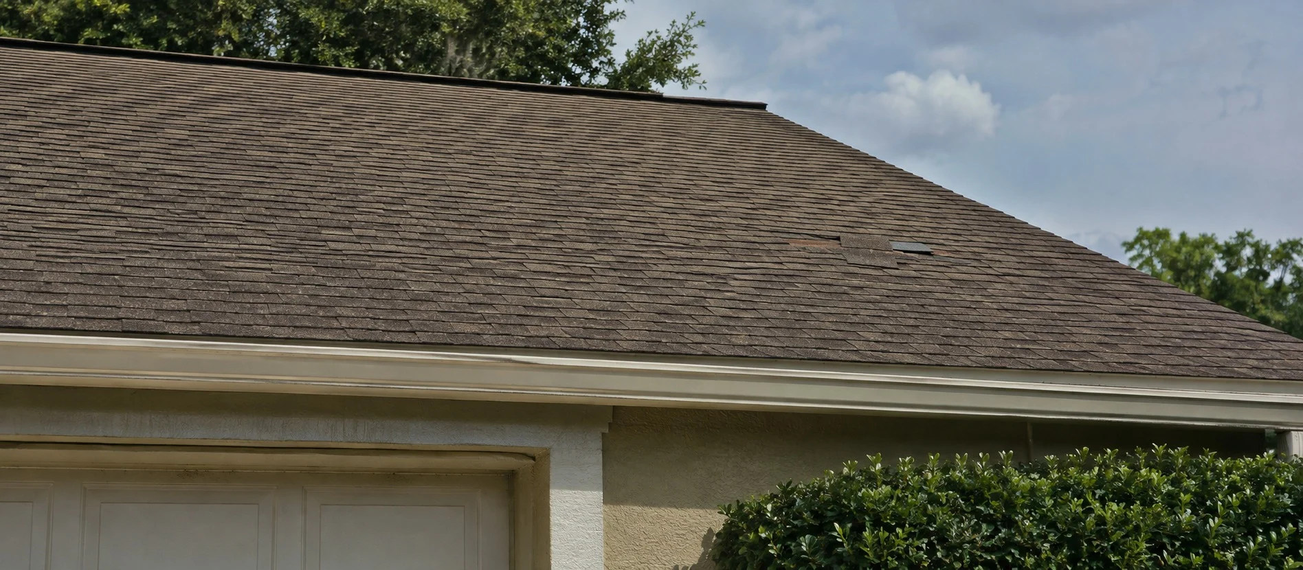 A patch of missing shingles on the roof above a garage.