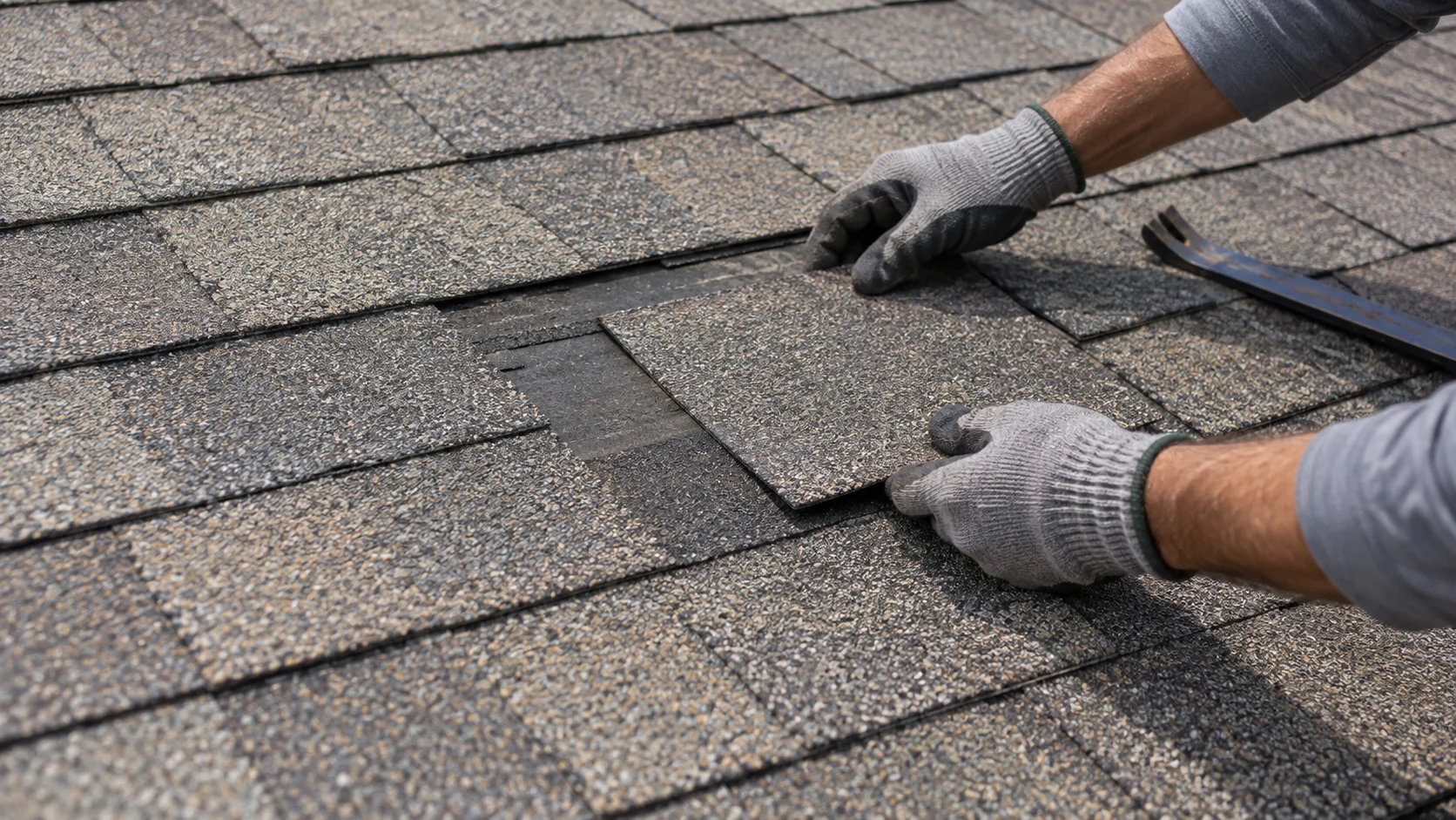 Gloved hands working on shingles during a roof repair.